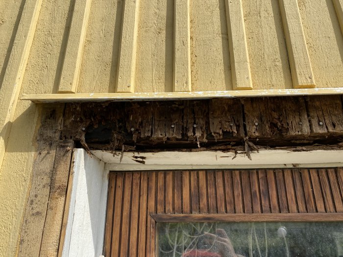 Rötskadade fasadbrädor ovanför en garageport på ett 50-tals hus.