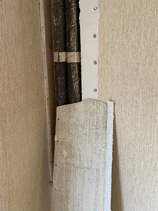 A partially removed wall panel revealing pipes behind it, possibly indicating asbestos concerns in a 1950s/60s apartment renovation.