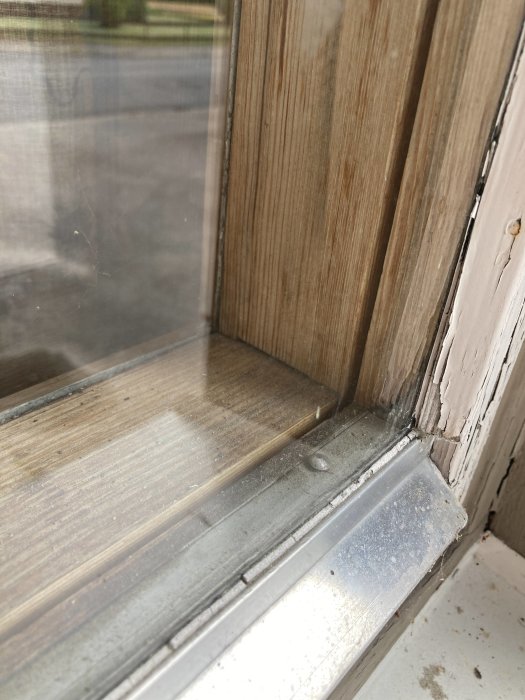 Närbild av ett fönsterhörn som visar träram och metallfönsterbänk, möjlig tecken på slitage eller fuktskada.
