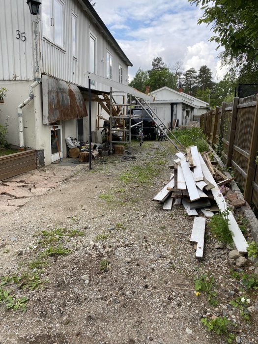 Oorganiserad uppfart med grus och byggavfall vid vitmålat hus med synlig balkongstruktur.