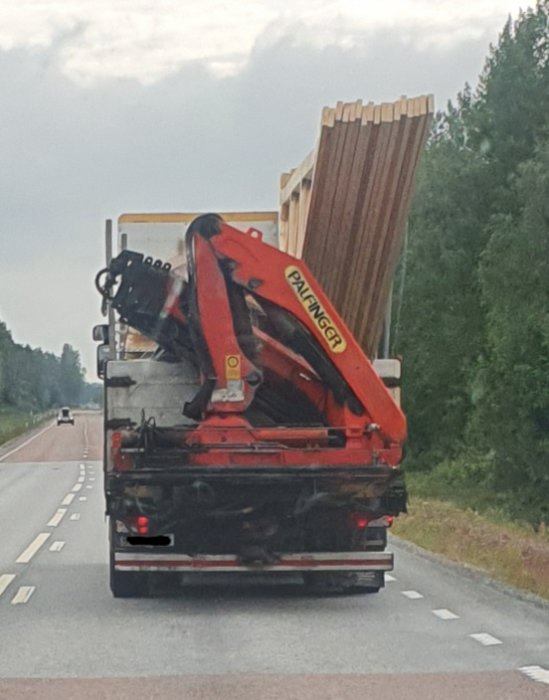 Lastbil med takstolar och byggmaterial säkrat med spännband på flak med en grävmaskin.