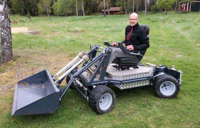 Person sitter i en helelektrisk 4WD och 4WS maskin med frontlastare på en gräsmatta.