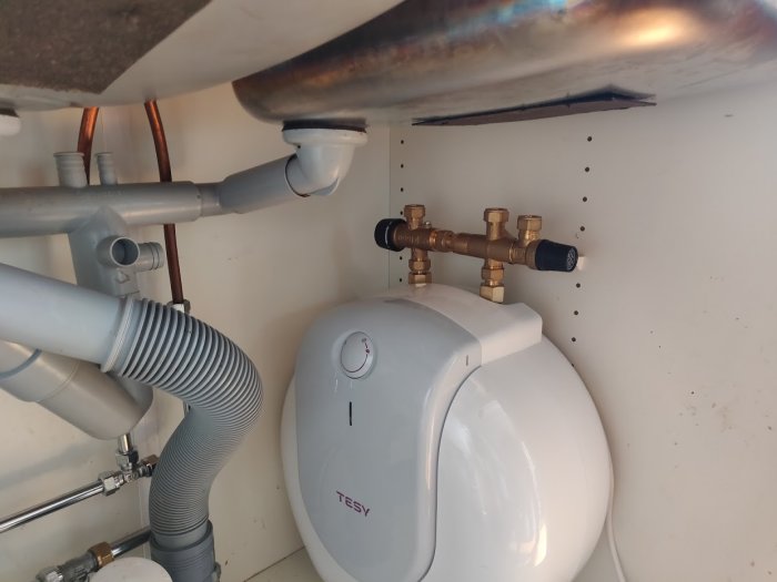 Varmvattenberedare med kopplade rör och ventilkombination under en diskbänk.