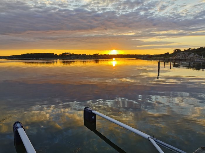 Solnedgång vid stilla hav med brygga och himmelsreflektioner i vattnet.