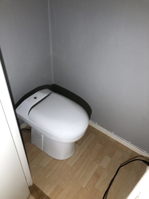 Nyinstallerad Wostman Ecodry toalett med porslinstol och separering i ett hörn av ett rum med trägolv.