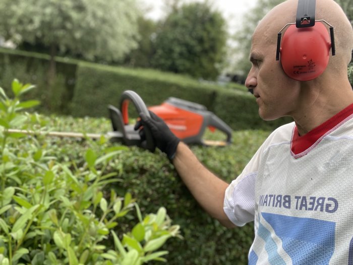 Person med hörselskydd klipper häcken med elektriska häcksaxar.