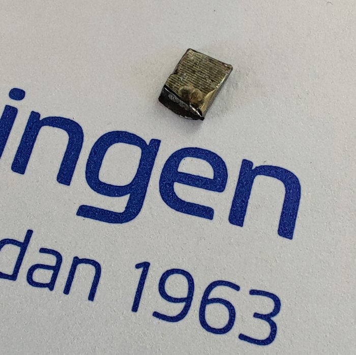 Liten lös metallbit på papper med blå text "ingenjören sedan 1963".