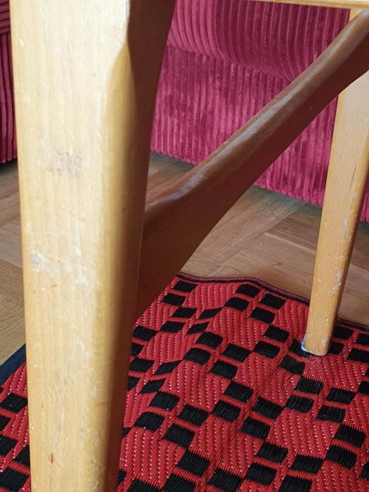Närbild på slitet träben av möbel mot röd sittkudde med skador och tecken på slitage.