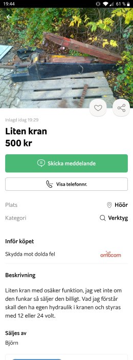 Begagnad liten kran med rost och slitage, oklar funktionalitet, säljs för 500 kr, bakgrund av buskar.