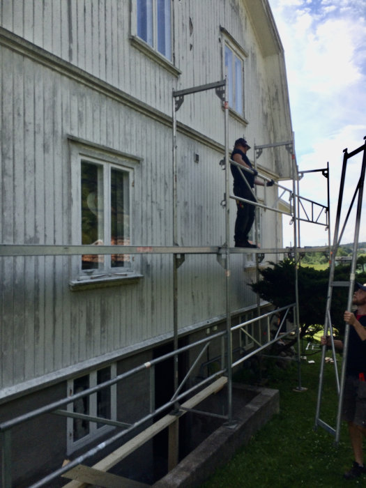 Underhållsmålning av bostadshusets fasad med två personer som sätter upp byggnadsställning.