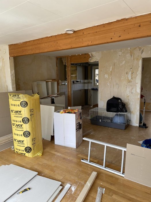 Bilde av et kjøkken under renovering med en synlig trebjelke i taket, fjernede gipsplater, og materialer stablet på gulvet.