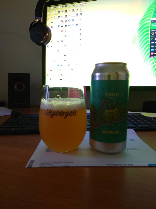 Ölglas med märket Stigbergets och burk av Verdant IPA framför en datorskärm och tangentbord.