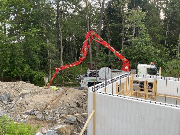 Betongpumpbil som häller betong i förberedda gjutformar på en byggarbetsplats med skog i bakgrunden.