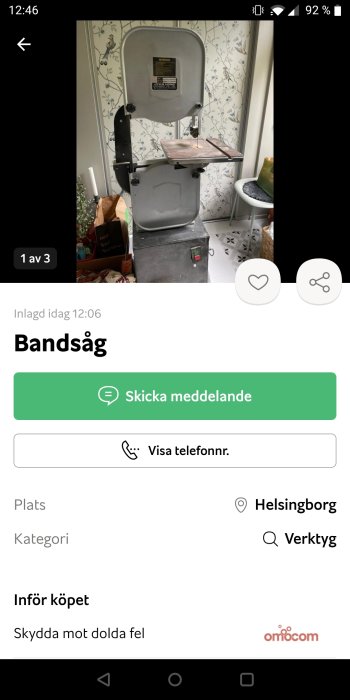 Bandsåg med grått stativ och träarbetsbord, placerad inomhus framför dekorerad vägg.