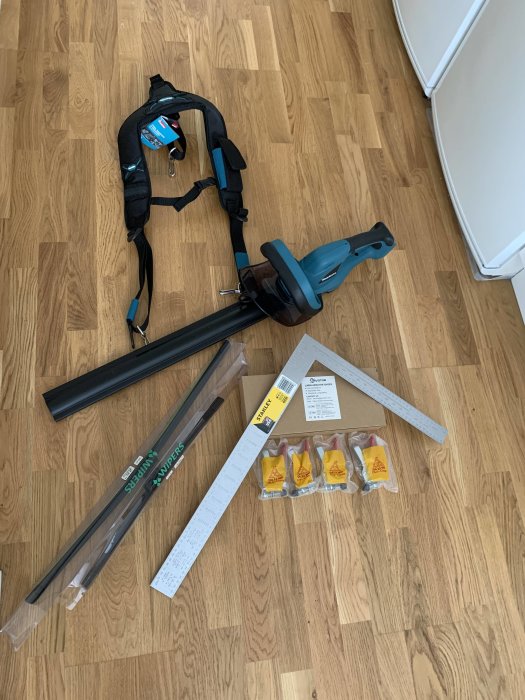 Verktyg och tillbehör på golv: häcksax, vinkelhake, spikskor, torkarblad, hängslen och vippklämmor.