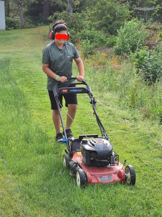 Person använder en bensindriven gräsklippare på en gräsmatta.