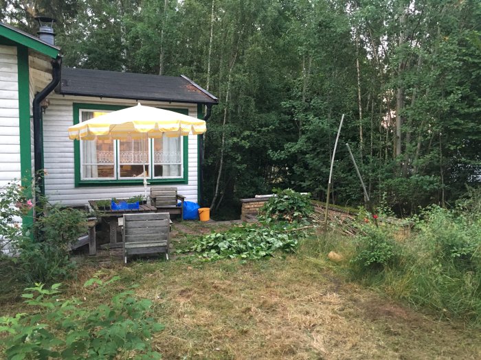 Exteriör av slitet sommarhus med trädgård och markis, potentiellt i behov av takrenovering.