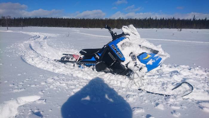 Blå och vit snöskoter välvd i snön med tydliga spår på en solig dag.