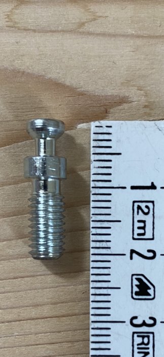 Fingängad skruv vid sidan av en linjal på ett träbord för storleksjämförelse.