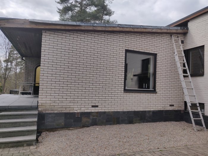 Bild på fasaden av ett hus från 1968 med vita tegel och en svart grund, stegar lutade mot väggen.