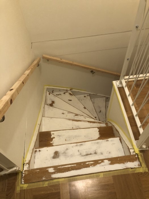En förberedd trätrappa med tejpade kanter och delvis bortslipad gammal färg, redo för målning.