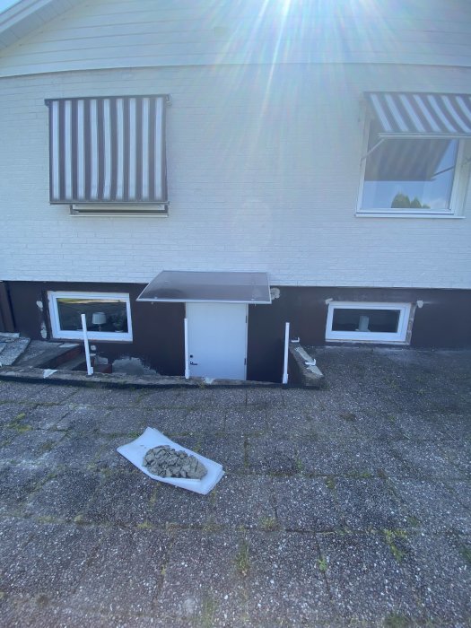 Husvägg nymålad i färg som uppfattas blågrå istället för ljusgrå, renoveringsmaterial synligt.