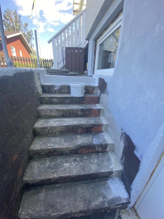 Trappsteg under målning med hink, där den ljusgrå färgen ser blåaktig ut mot husväggen.