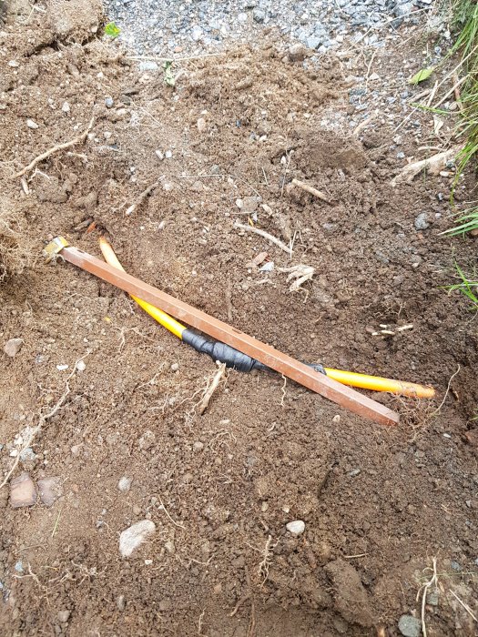 Elkabel skyddad med svart isolering grävd ner i jord med delvis synliga gula och orange ledningar.