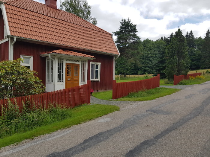 Nymålade röda grindstolpar vid en väg med en röd stuga i bakgrunden.