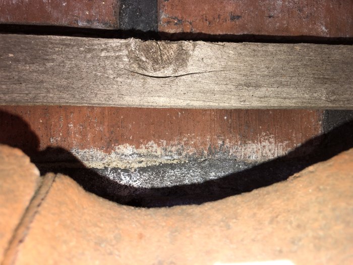 Närvaro av gammal, spröd plasttätning under nockpannor på ett tak, med synligt öppet utrymme och infällt dagsljus.