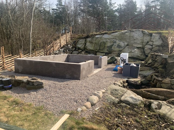 Nybyggt fundament för växthus med grusgång och stenmur i en trädgård.