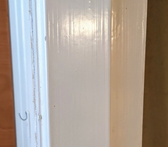 Närstående bild på en vitmålad dörrkarm i en 50-talslägenhet, med synliga tecken på demontering.