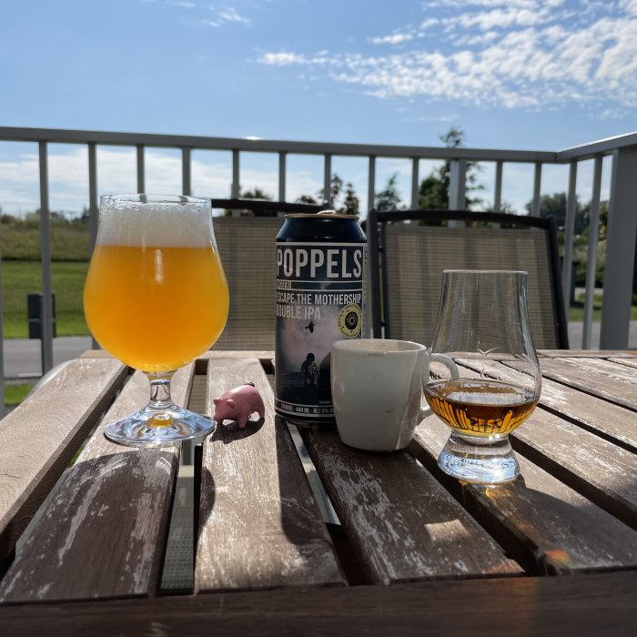 Ölglas och burk med Popppels Double IPA på ett utebord, espresso och whiskyglass mot solig himmel.