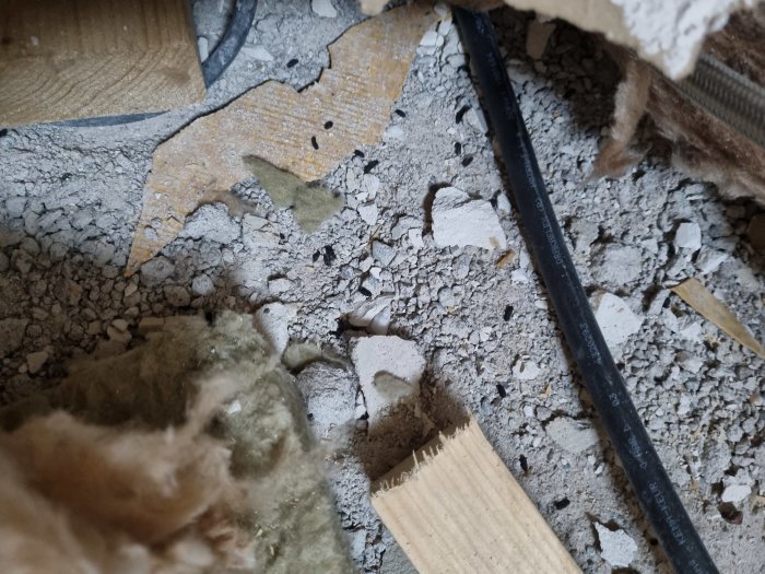Röran av gammal isolering, misstänkt råttbajs och rivningsavfall på ett betonggolv under renovering.
