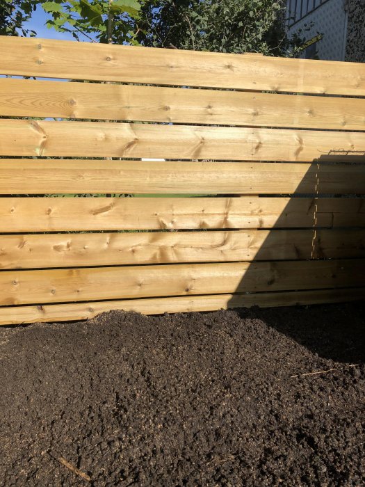 Nytt trästaket med horisontella plank och skugga. Jorden frampå för beplaning.