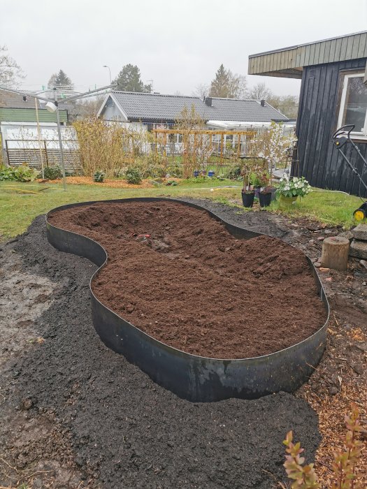 Böjd cortenkant i en trädgård, fylld med jord, klar för plantering.