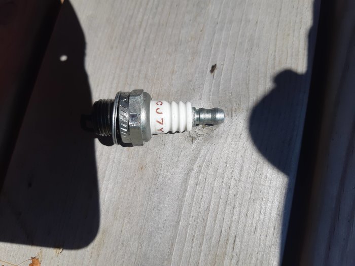 Tändstift på träbakgrund, uttaget för byte eller kontroll från röjsåg som inte startar.