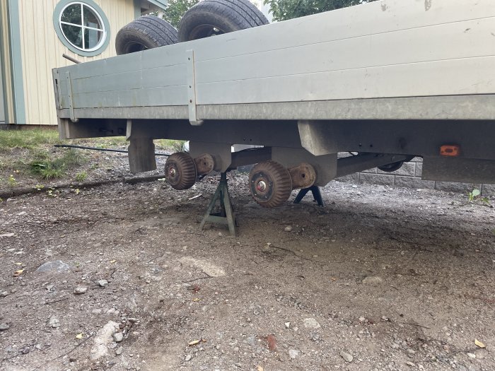 Släpvagn uppallad på stödben utan hjul, bredvid dubbade reservhjul lutade mot släpets sida.