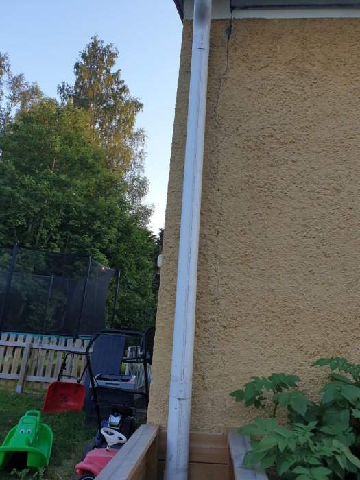 Lång spricka längs ytterväggen på huset nära ett rör, från tak till marknivå.