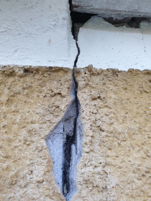 En stor spricka i en husvägg från nock till grund av lättbetongblock, med puts som lossnat.