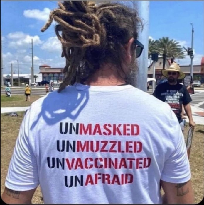 Person bakifrån med dreadlocks och T-shirt med texten "UNMASKED UNMUZZLED UNVACCINATED UNAFRAID