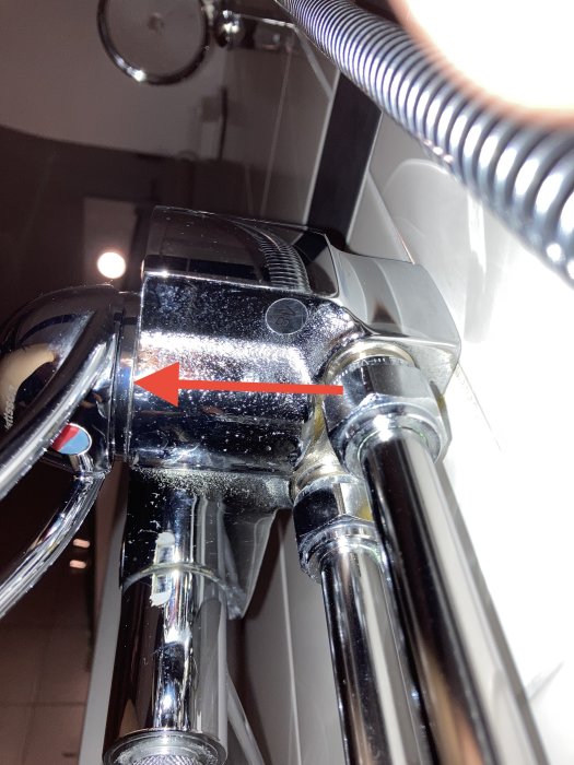 Duschblandare med en pil som visar var det droppar bakom vredet, antydan till vattenläckage.