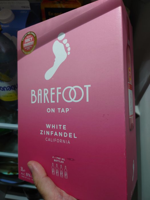 Hand håller en rosa box med Barefoot White Zinfandel vin i ett kylskåp.