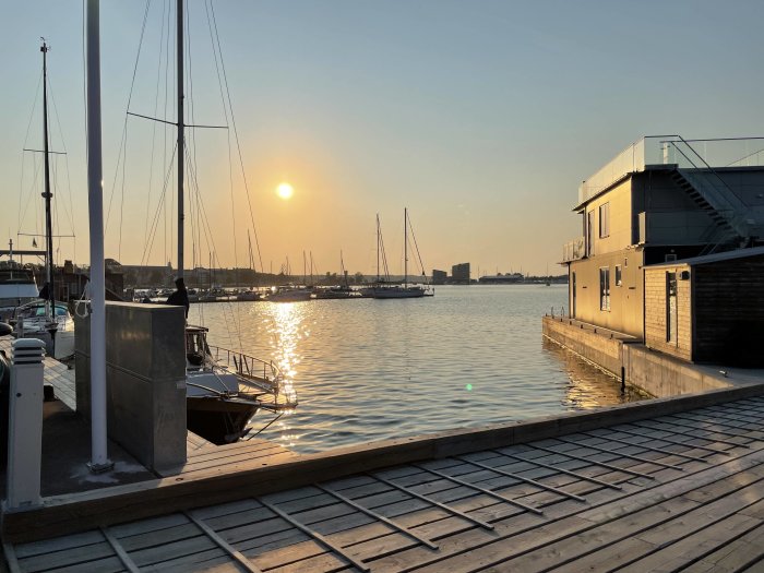 Solnedgång vid Västerviks småbåtshamn med båtar och flytande bostadshus.