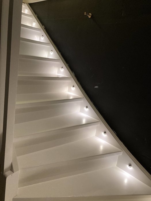 Vit trappa med Gelia Stairlight Spotlight på varje steg som ger stark belysning.