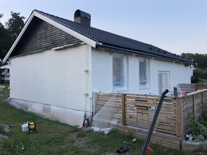 Nymålat vitt hus med sprayutrustning och skyddad framsida, delvis täckt plank och trädgårdsslang.