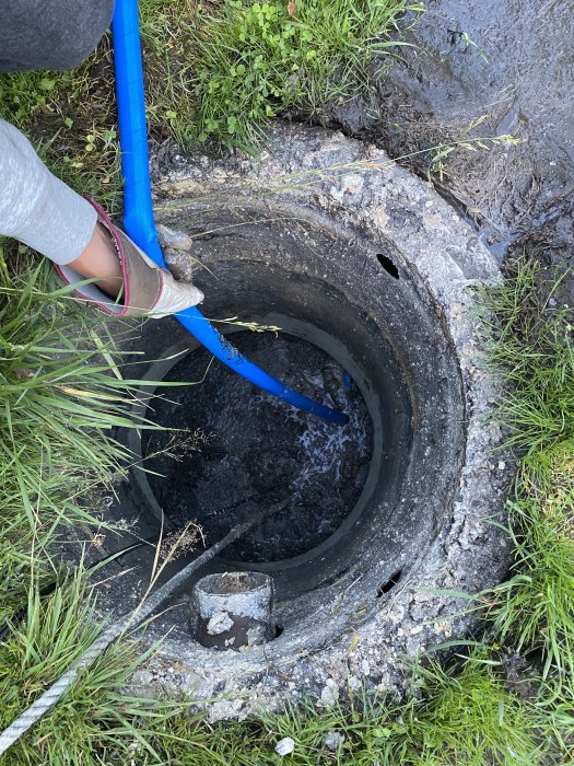 En person tömmer en brunn med en blå slang, brunnens konstruktion är synlig.