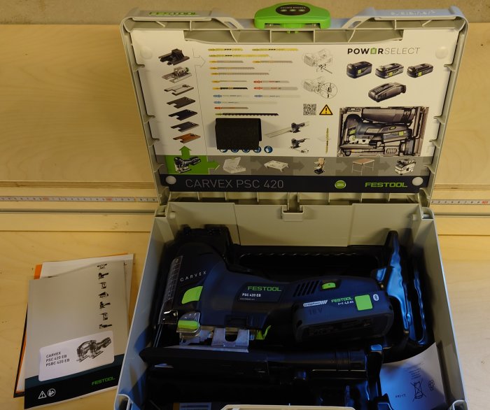 Öppen verktygslåda med en Festool Carvex PSC 420 sticksåg och 4,0 Ah 18V batteri, bruksanvisningar och tillbehör.