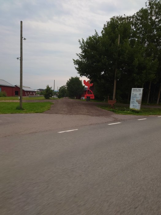 Vägkorsning med röd skulptur av en älgtjur och informationsskylt vid sidan av vägen.