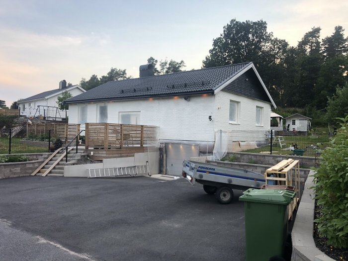 Vitmålat hus med nymålad fasad och nytt trädäck, byggmaterial och släpvagn framför huset.